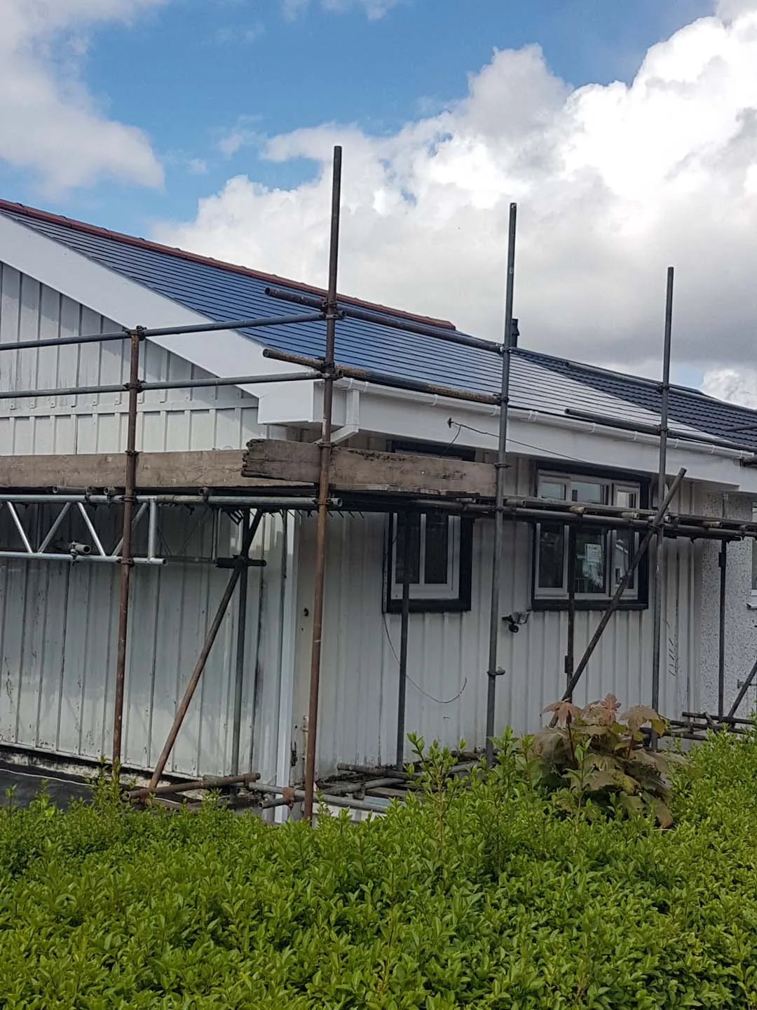 Bungalow with new slate roof, white fascias, soffits and gutters behind scaffolding