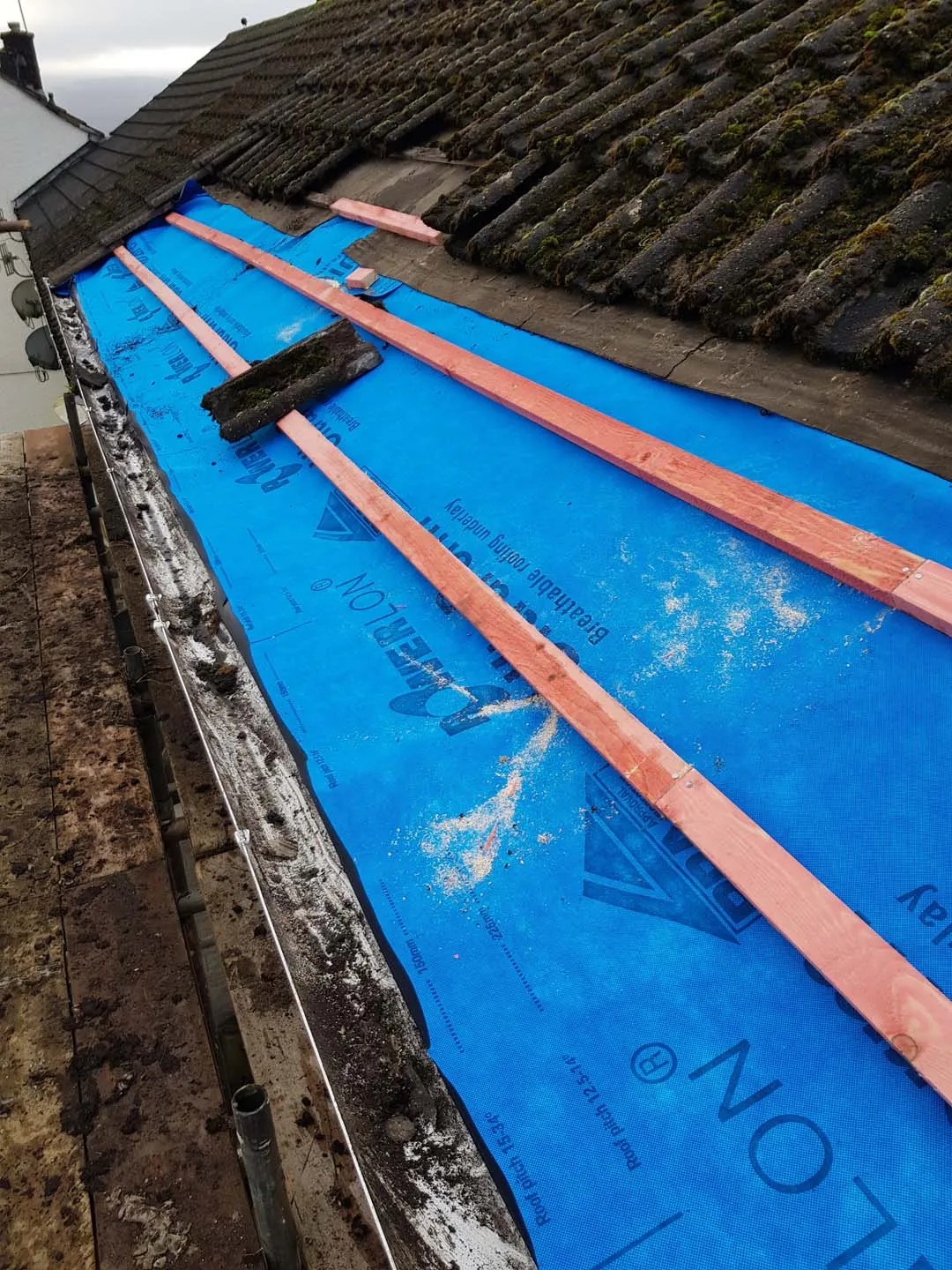 Lower courses of a tiled roof stripped, with new blue breathable membrane and new treated battens along the eaves