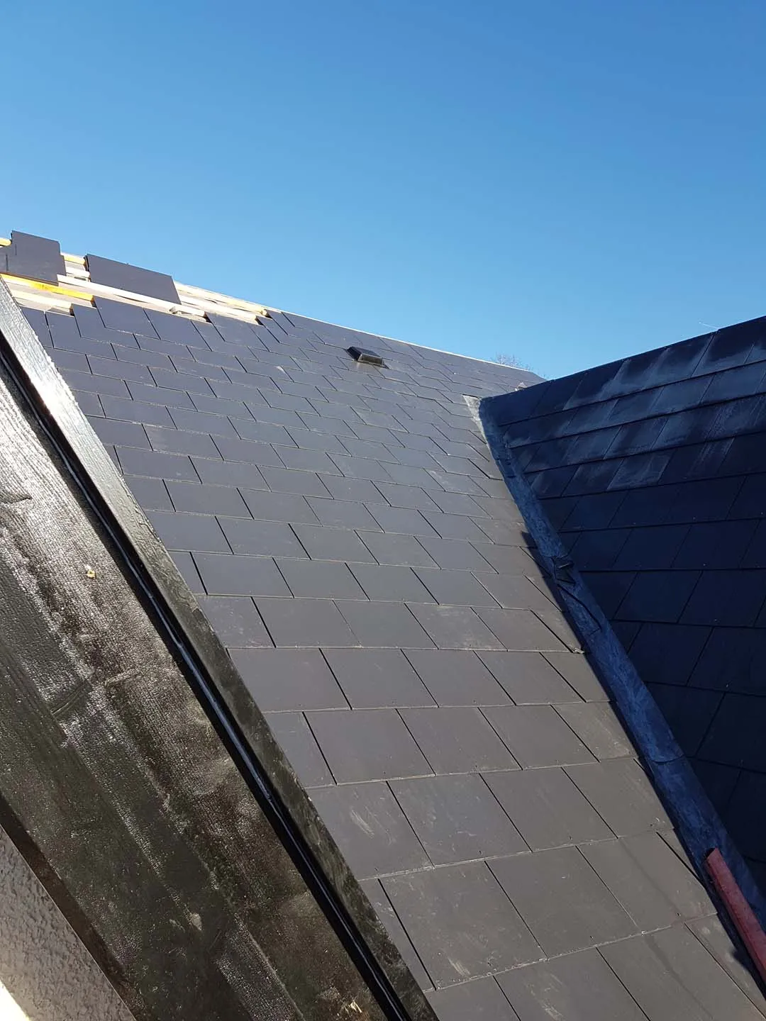 Newly slated roof slope with black bargeboard and lead valley under a blue sky